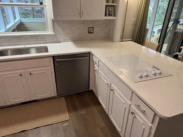 White kitchen cabinets with a new white countertop, cooktop and stainless dishwasher