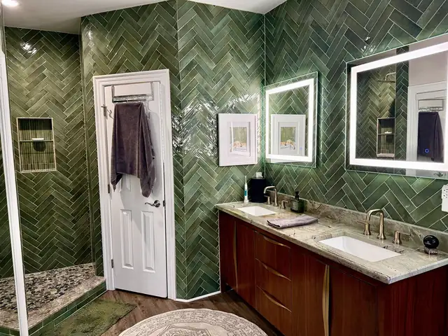 Master bathroom with green herringbone wall tile, a dark wood double vanity with granite top and lighted mirrors