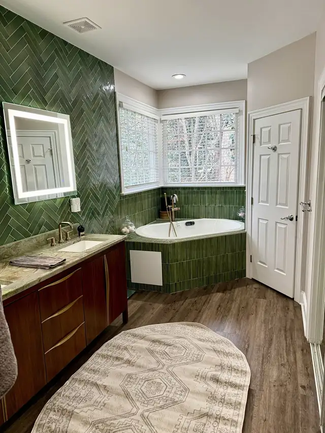 Green herringbone tile bathroom with a corner tub, wood vanity and window