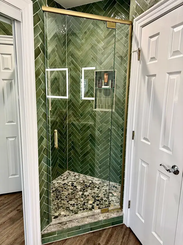 Walk-in shower with green herringbone tile, two lighted niches, pebble floor and frameless glass door